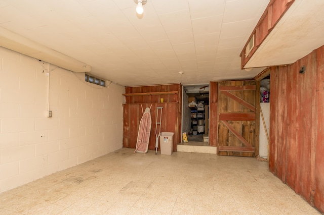 finished basement with concrete block wall, wooden walls, and tile patterned floors