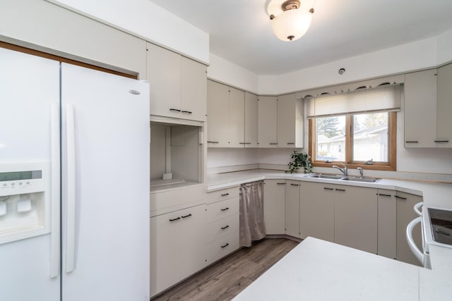 kitchen with a peninsula, white appliances, wood finished floors, a sink, and light countertops