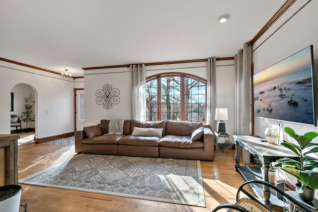 living room featuring crown molding, baseboards, arched walkways, and light wood finished floors