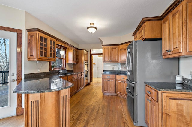 kitchen with brown cabinetry, a peninsula, light wood-style flooring, a sink, and glass insert cabinets