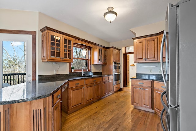 kitchen with brown cabinets, light wood-style flooring, a sink, stainless steel appliances, and glass insert cabinets