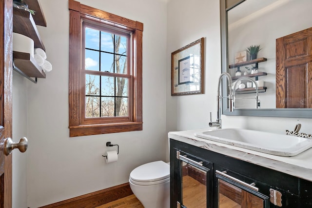 half bath with baseboards, toilet, wood finished floors, and vanity