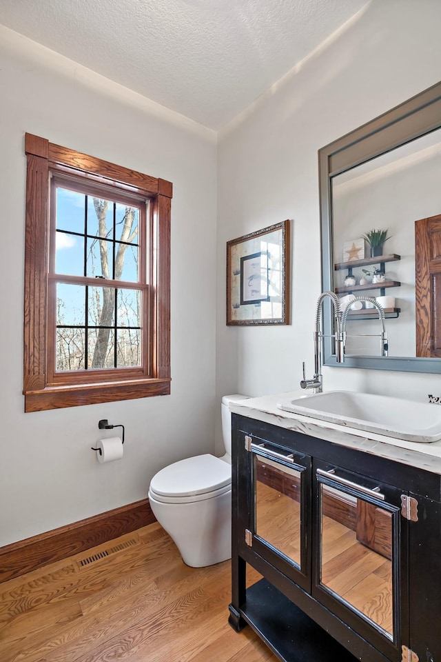 half bath with visible vents, toilet, a textured ceiling, wood finished floors, and vanity