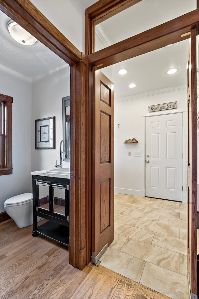 bathroom featuring toilet, wood finished floors, crown molding, baseboards, and vanity