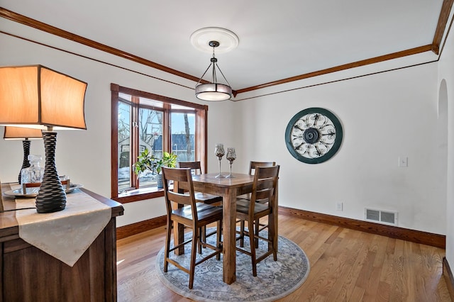 dining area with crown molding, baseboards, visible vents, and light wood finished floors