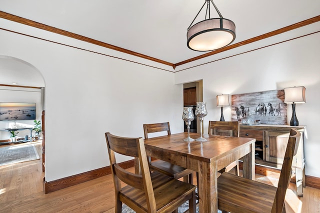 dining room with arched walkways, baseboards, light wood-type flooring, and ornamental molding