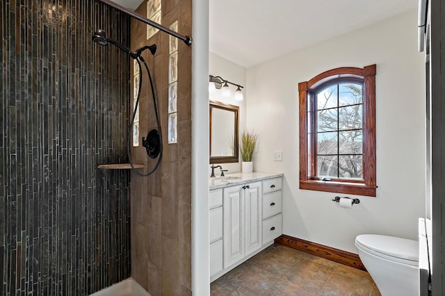 full bathroom featuring toilet, tiled shower, vanity, and baseboards