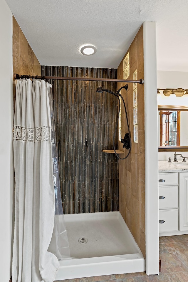 bathroom with a textured ceiling, vanity, and tiled shower