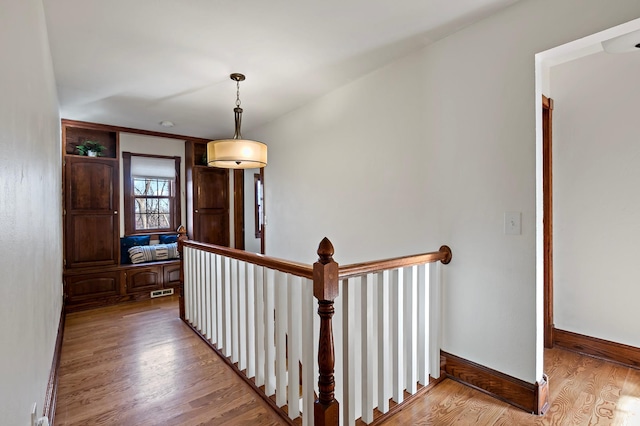 hall with an upstairs landing, visible vents, baseboards, and wood finished floors