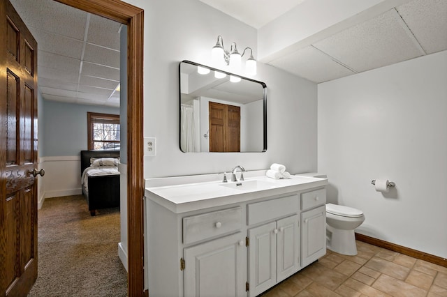 bathroom featuring a drop ceiling, baseboards, toilet, and vanity