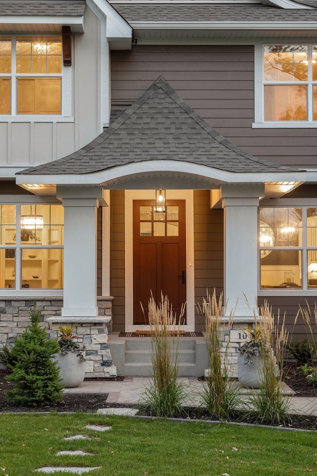 property entrance with covered porch, stone siding, and roof with shingles