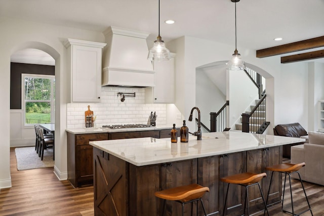 kitchen featuring light stone counters, premium range hood, dark wood-style flooring, white cabinets, and tasteful backsplash