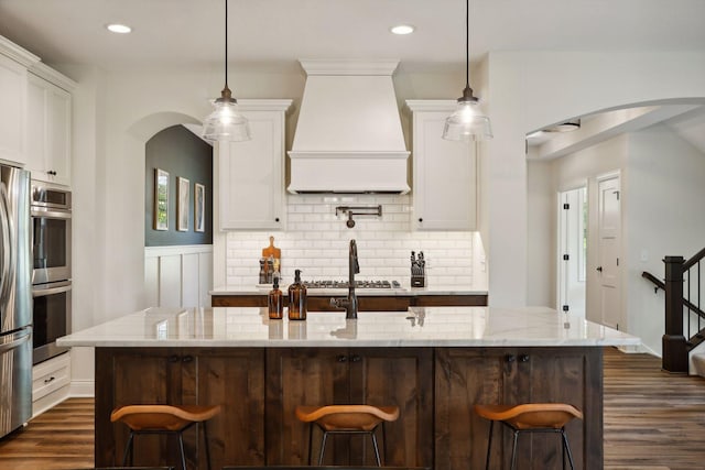 kitchen with appliances with stainless steel finishes, tasteful backsplash, premium range hood, and white cabinetry