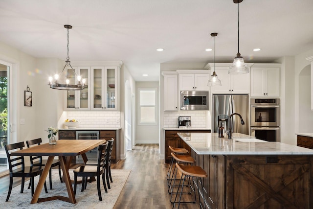 kitchen with dark wood-style flooring, a center island with sink, stainless steel appliances, glass insert cabinets, and a sink