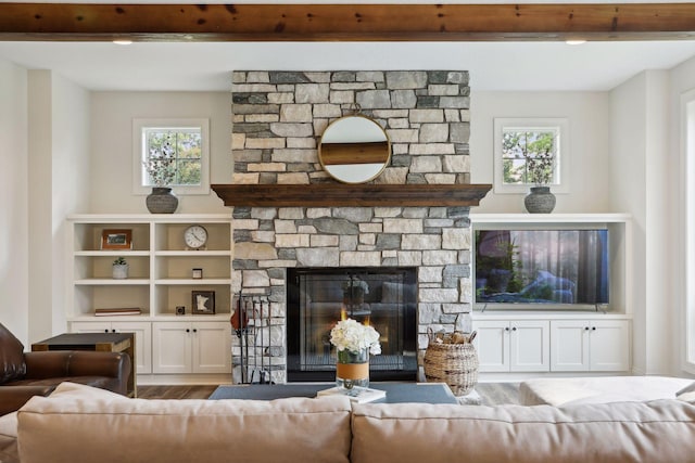 living area with a healthy amount of sunlight, beam ceiling, wood finished floors, and a stone fireplace