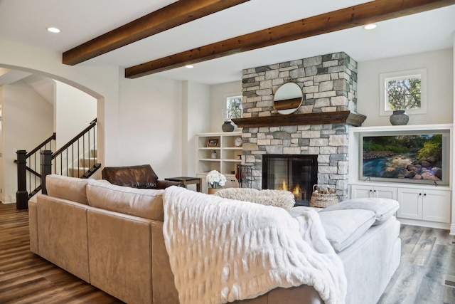 living room featuring beamed ceiling, wood finished floors, stairs, a stone fireplace, and recessed lighting