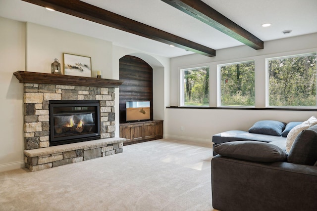 living area featuring carpet floors, beamed ceiling, a stone fireplace, and baseboards