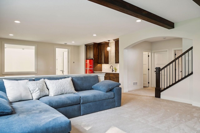 living room featuring arched walkways, light colored carpet, stairway, and baseboards