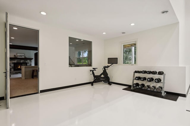 exercise room featuring a healthy amount of sunlight, visible vents, a stone fireplace, and recessed lighting