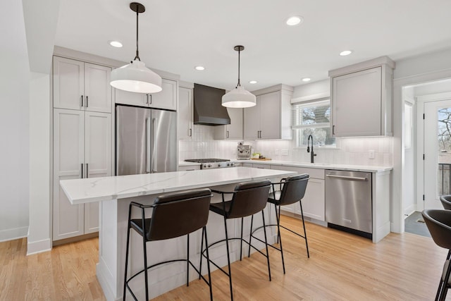 kitchen featuring a kitchen island, a breakfast bar, stainless steel appliances, wall chimney exhaust hood, and light wood-type flooring