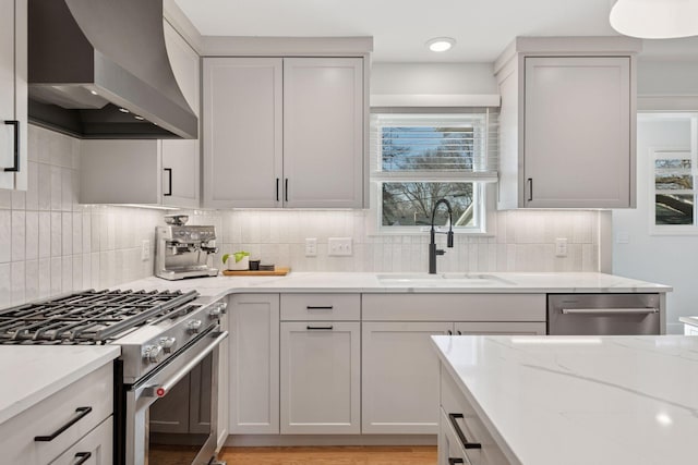 kitchen featuring light stone counters, decorative backsplash, appliances with stainless steel finishes, wall chimney exhaust hood, and a sink