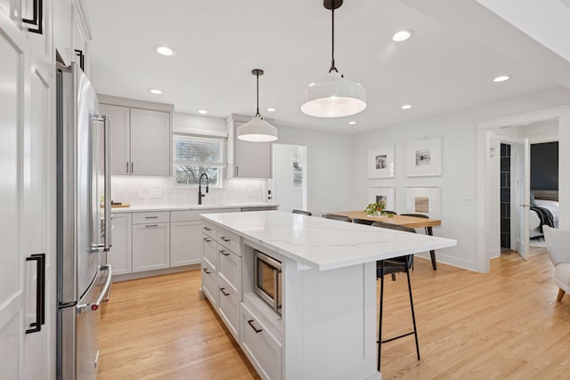 kitchen featuring a kitchen bar, light wood-style flooring, a sink, tasteful backsplash, and stainless steel appliances