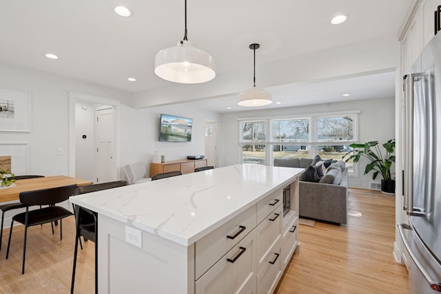 kitchen featuring a center island, open floor plan, high end refrigerator, light wood-style floors, and hanging light fixtures