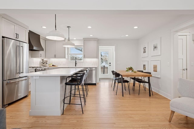 kitchen with a kitchen bar, wall chimney range hood, tasteful backsplash, appliances with stainless steel finishes, and light countertops