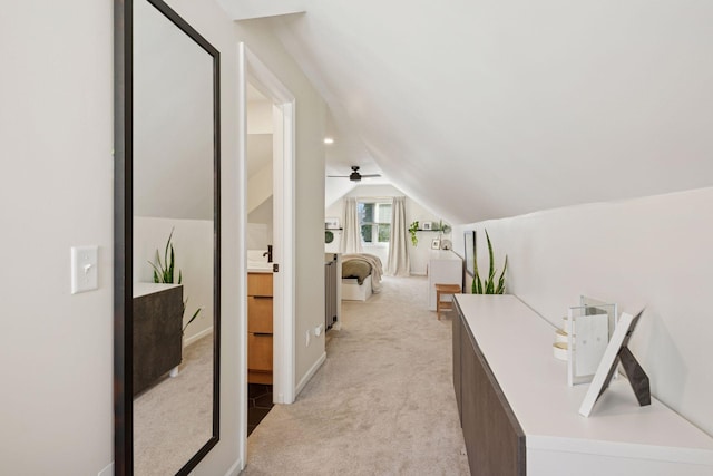 corridor featuring baseboards, light carpet, and vaulted ceiling