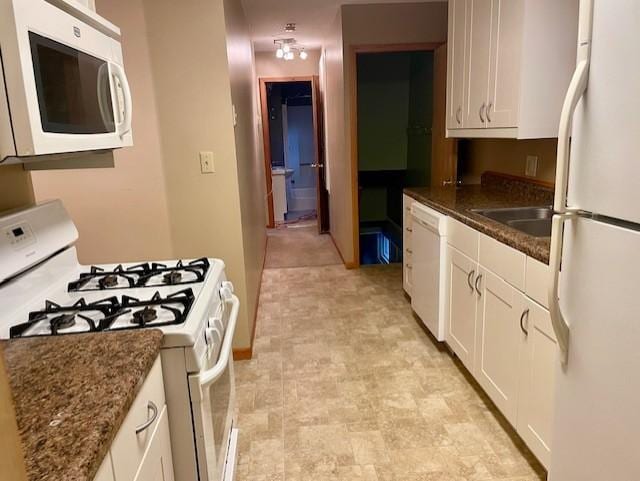 kitchen with white cabinetry, white appliances, dark stone countertops, and a sink