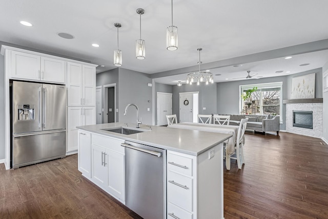 kitchen featuring dark wood finished floors, open floor plan, a stone fireplace, stainless steel appliances, and a sink