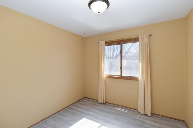 empty room with light wood-style floors, visible vents, and baseboards