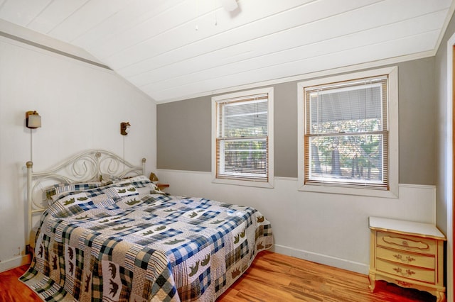 bedroom with light wood-style flooring, vaulted ceiling, and wainscoting