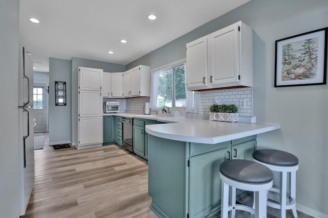 kitchen featuring a peninsula, light wood-style flooring, white cabinets, and backsplash