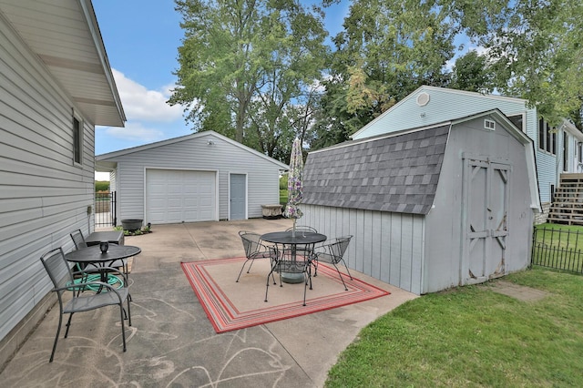 view of patio with an outdoor structure, driveway, a detached garage, and fence