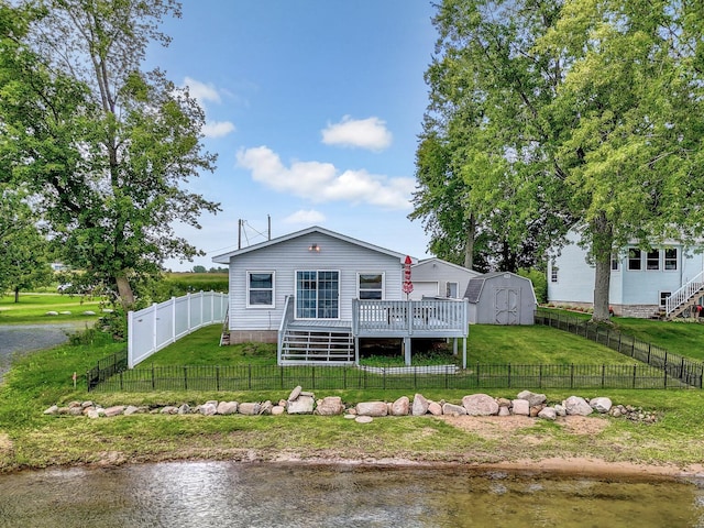 back of property with a lawn, a fenced backyard, an outbuilding, a deck with water view, and a shed