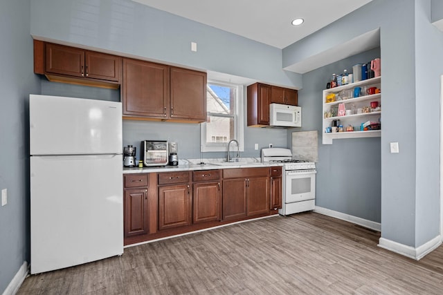 kitchen featuring light countertops, a sink, light wood-type flooring, white appliances, and baseboards