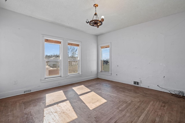 empty room with a textured ceiling, wood-type flooring, visible vents, and a notable chandelier