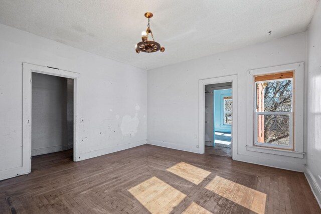 unfurnished room with a textured ceiling, hardwood / wood-style floors, an inviting chandelier, and baseboards