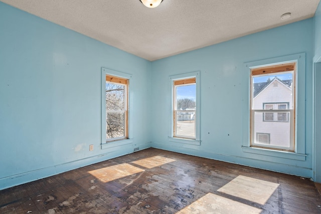 spare room with a textured ceiling, hardwood / wood-style floors, and baseboards