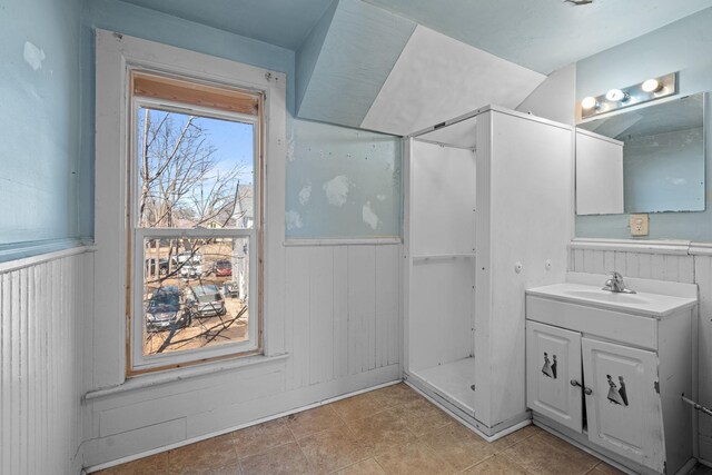 bathroom with a wainscoted wall, walk in shower, and vanity