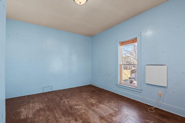 spare room with wood-type flooring, visible vents, and baseboards