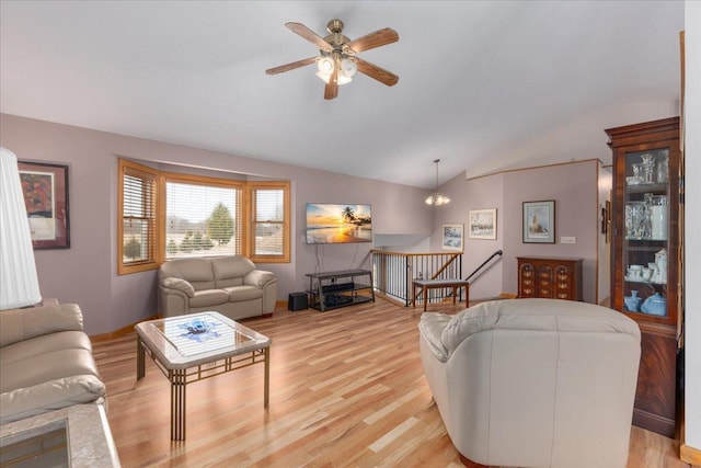 living area with lofted ceiling, ceiling fan with notable chandelier, light wood-style flooring, and baseboards