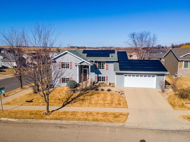 split foyer home featuring a garage, a shingled roof, concrete driveway, a residential view, and roof mounted solar panels