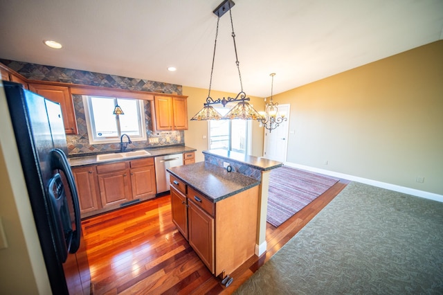 kitchen with dark countertops, a sink, dishwasher, baseboards, and black fridge