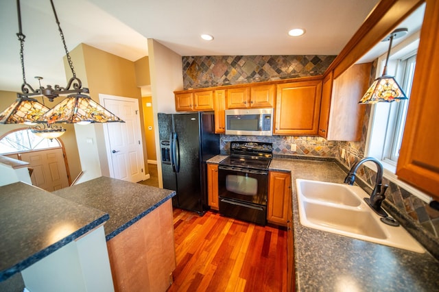 kitchen with dark countertops, a sink, light wood finished floors, and black appliances