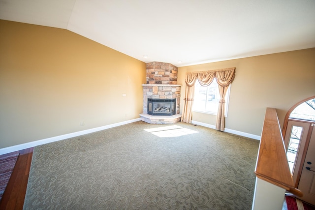 unfurnished living room with lofted ceiling, a stone fireplace, carpet flooring, and baseboards