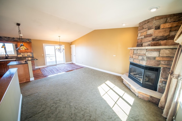 carpeted living area with lofted ceiling, a fireplace, baseboards, and a sink