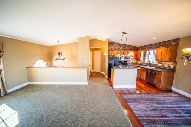 kitchen featuring dark countertops, lofted ceiling, black fridge with ice dispenser, stainless steel dishwasher, and a sink