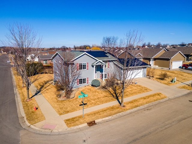 view of front of house featuring a garage, driveway, solar panels, and a residential view